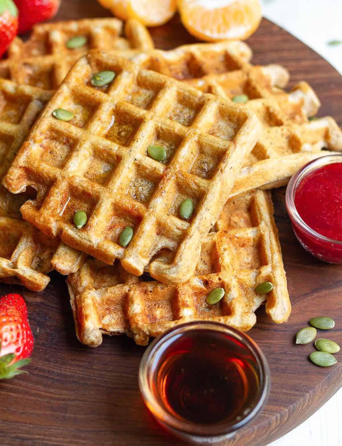 Carrot waffles topped with pumpkin seeds on a wooden board.