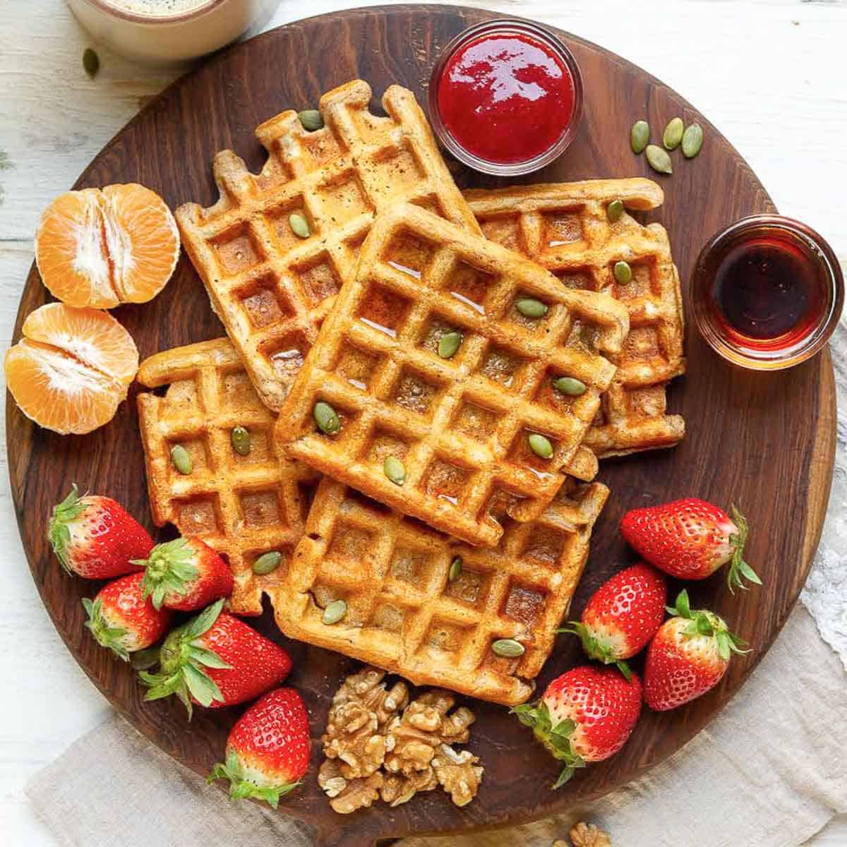 Waffles on a wooden board with fruits, walnuts, and maple syrup.