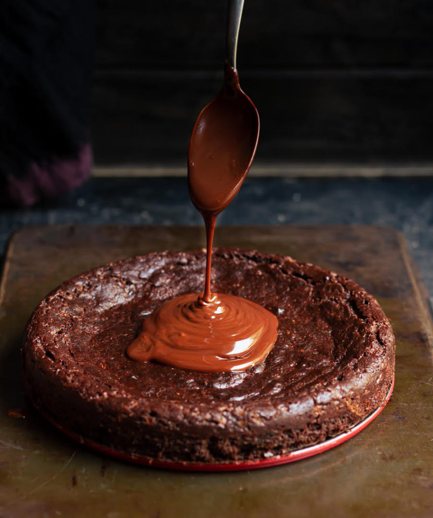 Chocolate sauce being poured on the cake with a spoon.