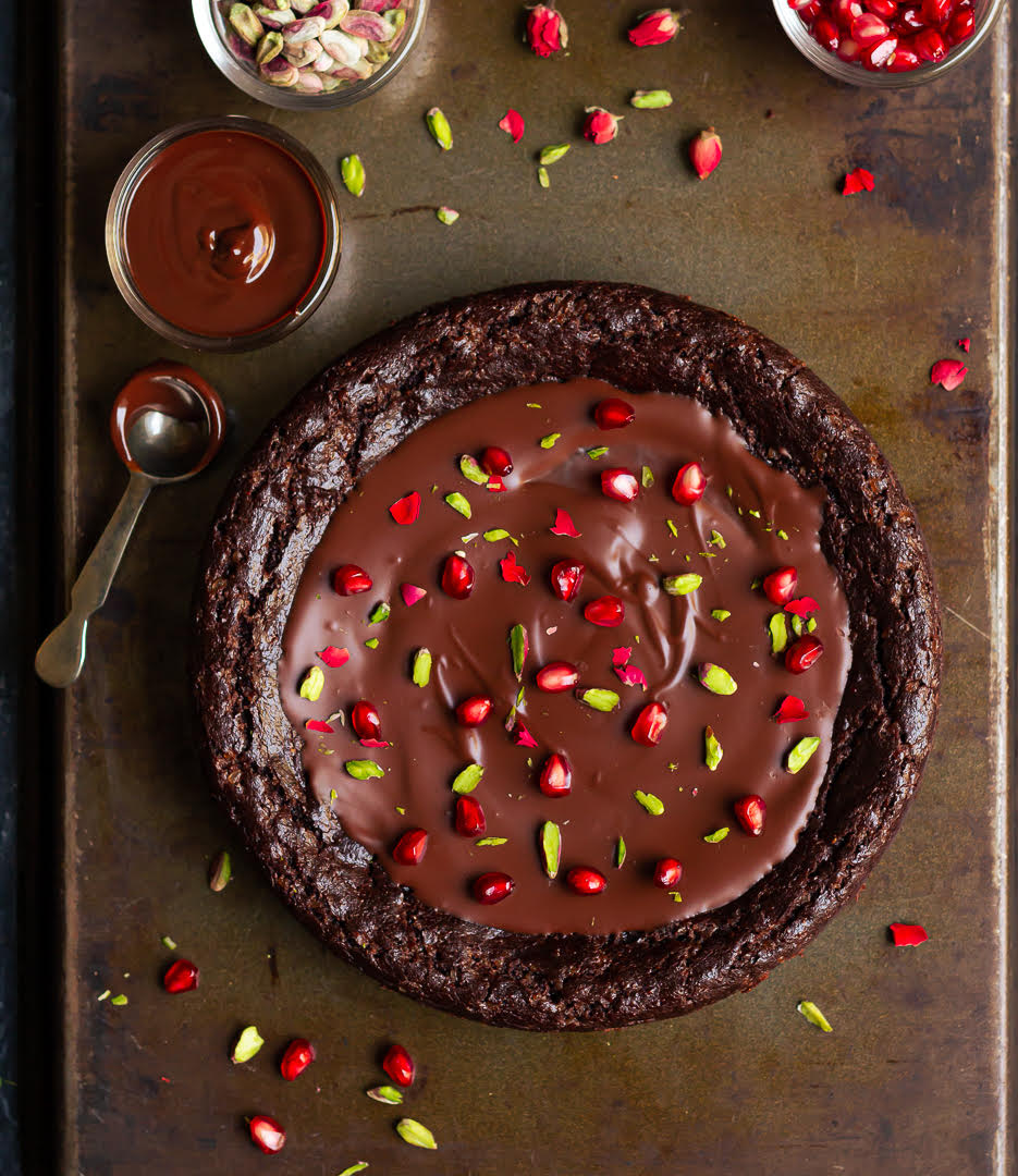 chocolate cake with ganache, pistachios and pomegranates on a tray.