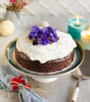 Rich chocolate zucchini cake with frosting on a cake stand.