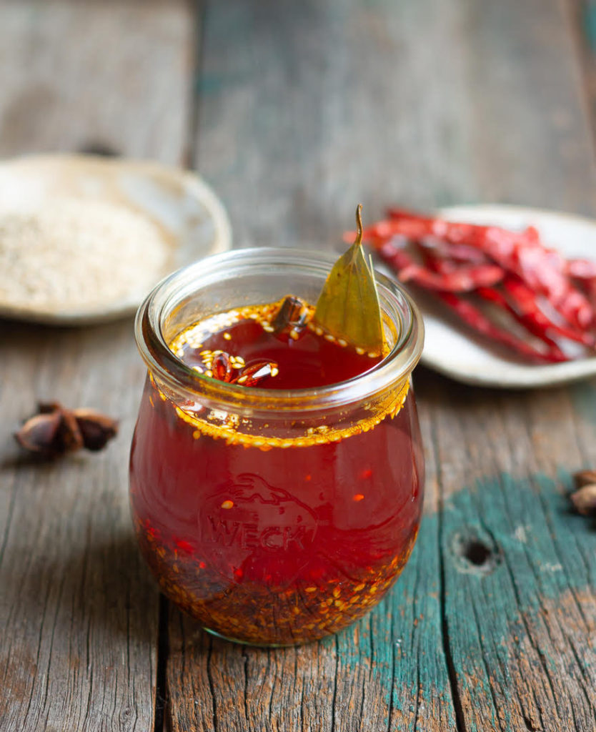 Chili oil in a glass jar on a wooden surface.