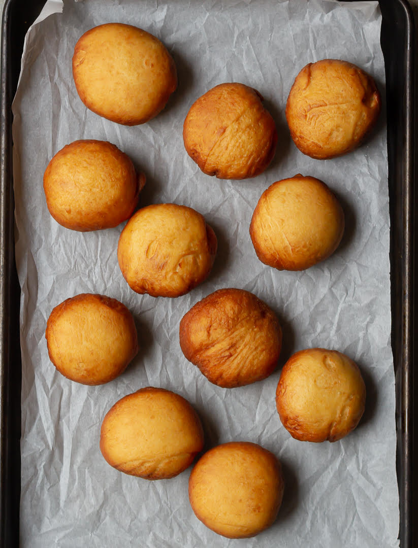 Fried donuts on parchment paper lined tray.