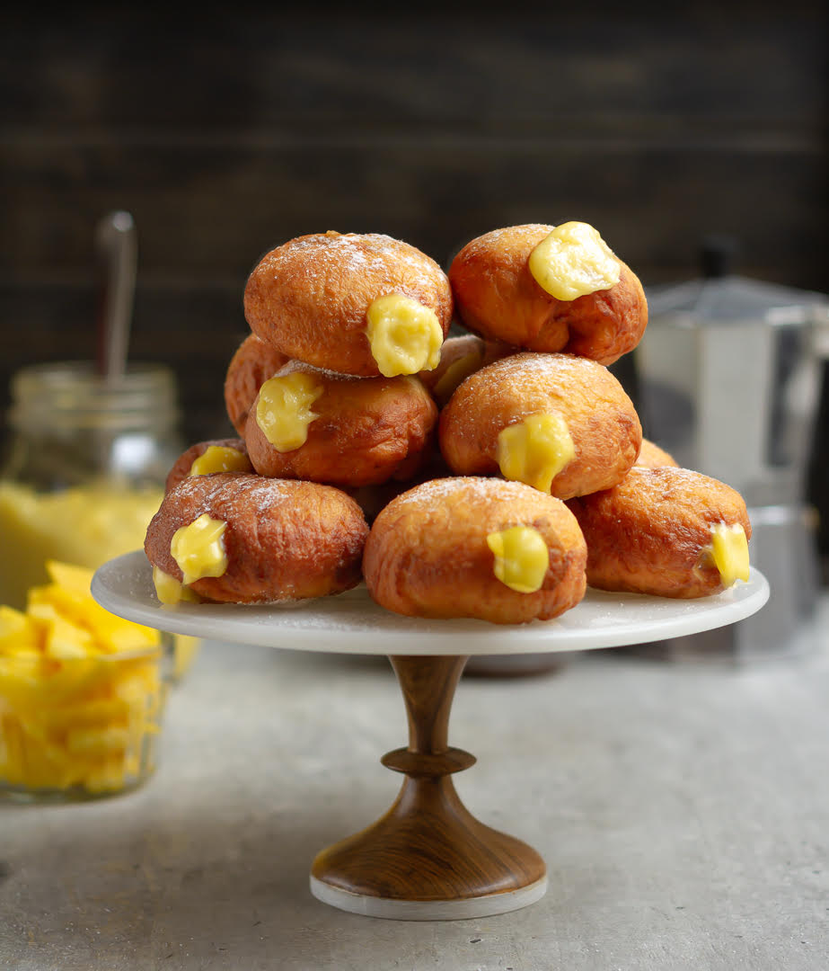 Donuts filled with mango curd stacked on a cake stand with ingredients in the background.