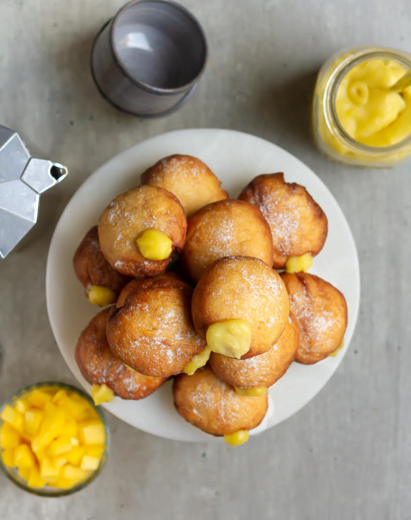 Mango bombolinis on a cake stand with ingredients around.