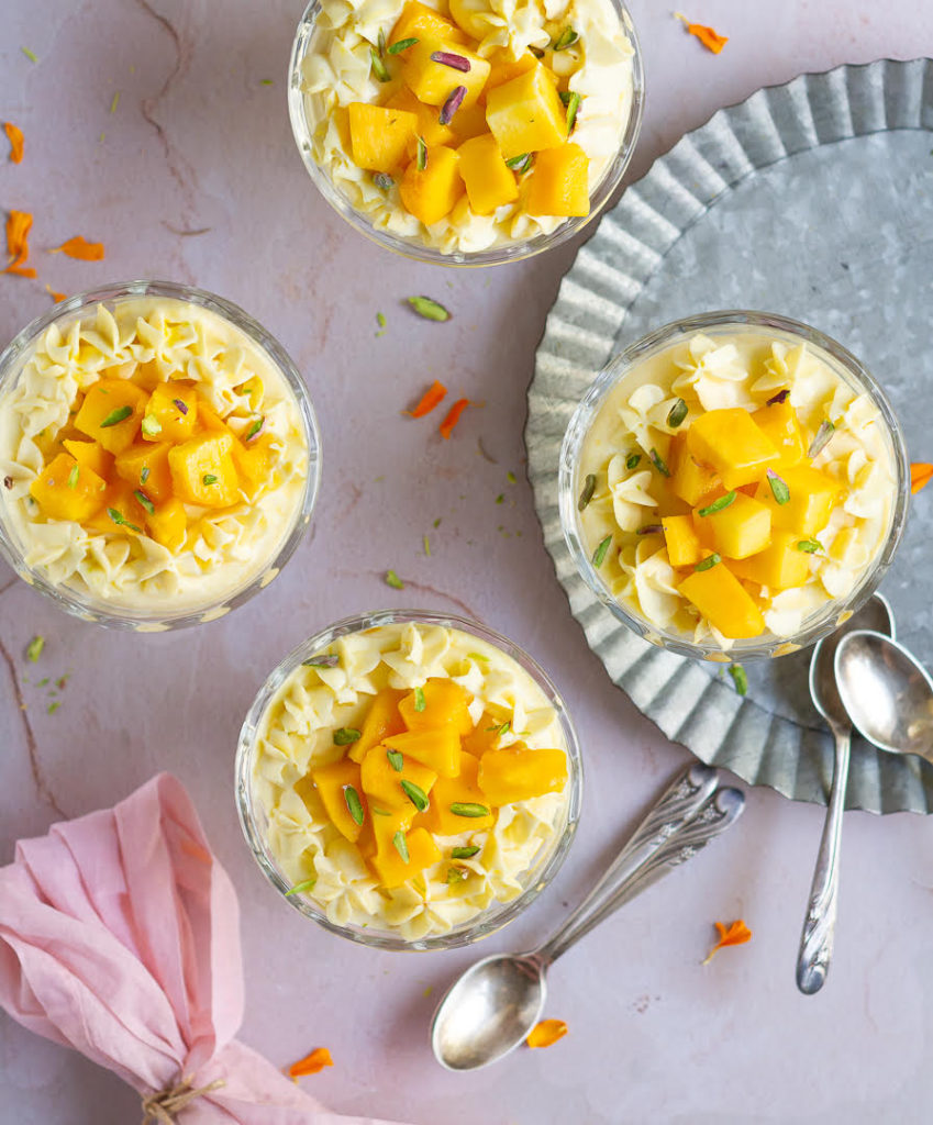 4 dessert bowls filled with mango cheesecake with spoons and a pink napkin on the side.