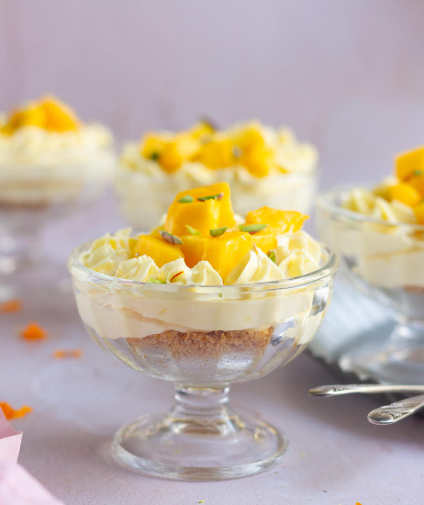 Mango Cheesecake in a dessert cup, garnished with mangoes and pistachios.