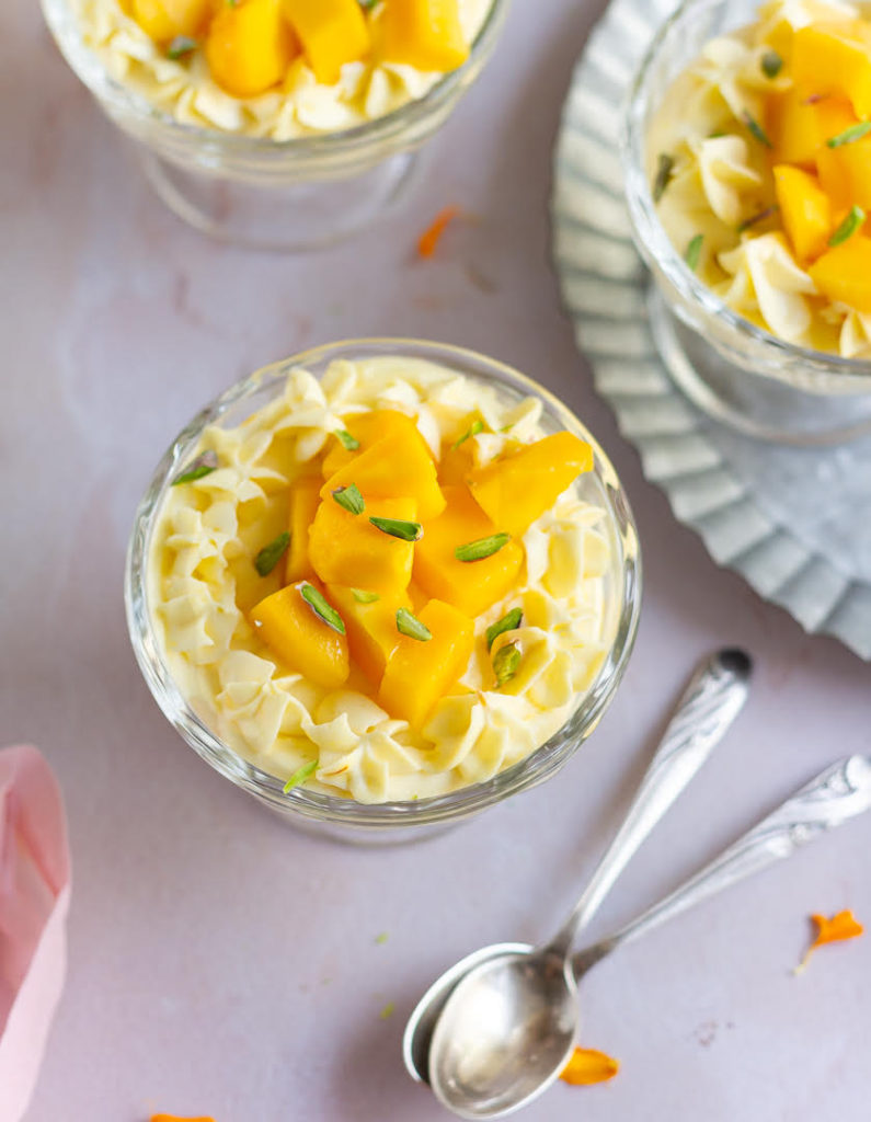No-bake mango cheesecake in a dessert cup with 2 spoons on the side.