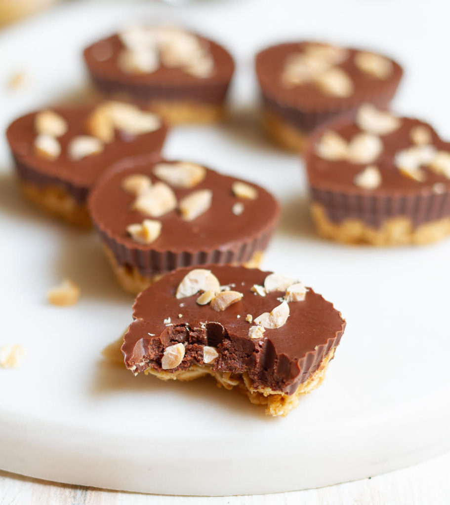 Peanut Butter Chocolate Oat Cups on a white tray with one half eaten peanut butter cup