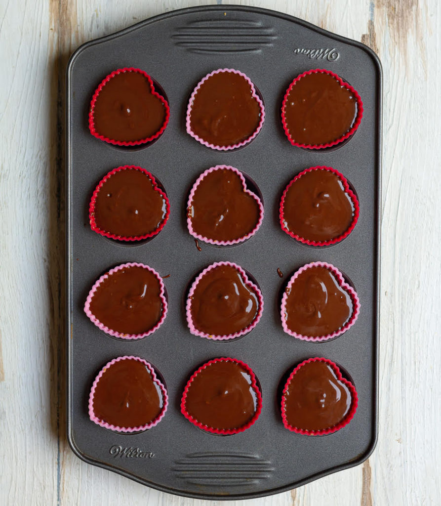 melted chocolate and peanut butter mixture on the oats base in silicon cups in a mini muffin tray
