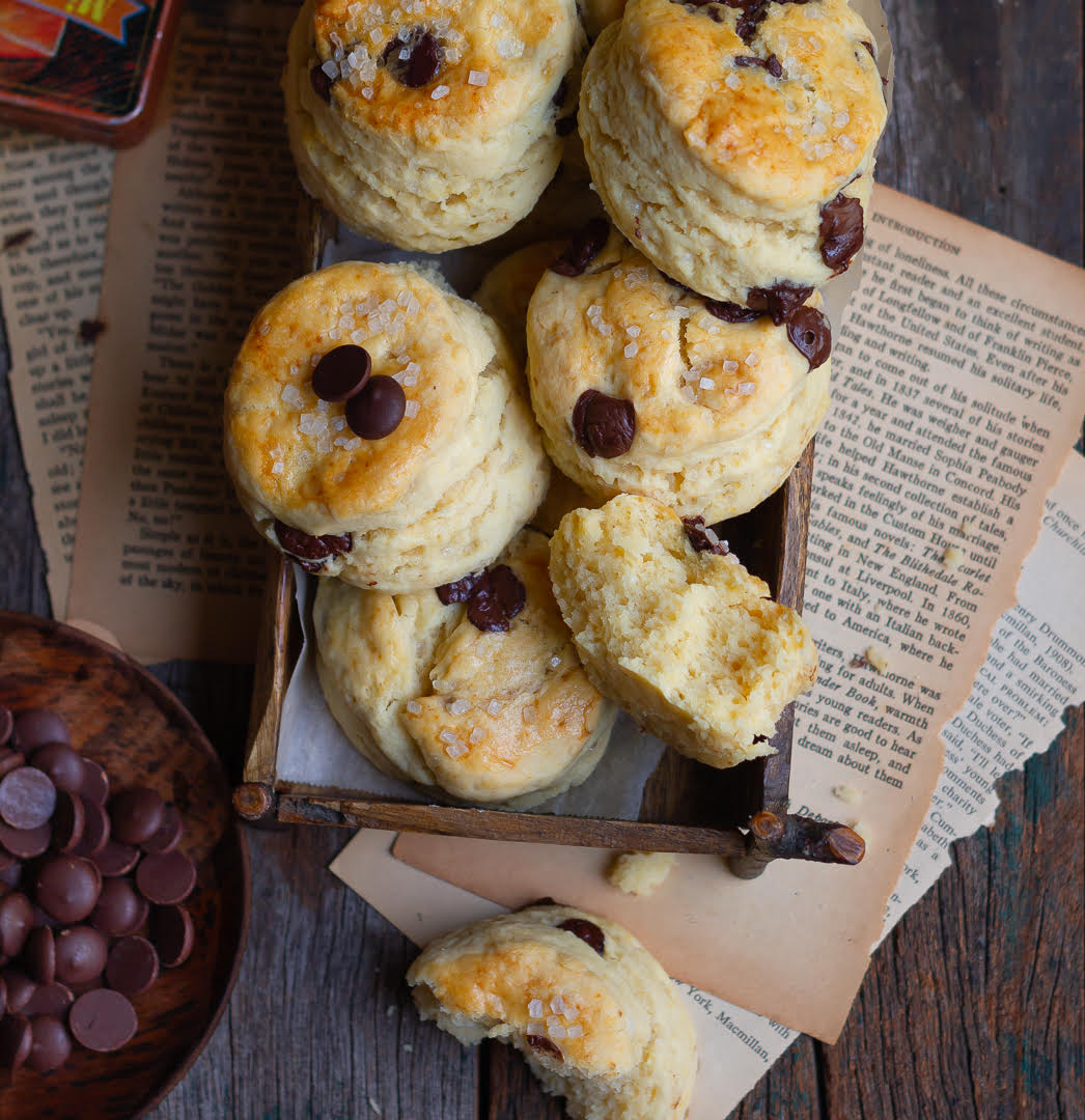 Chocolate chip scones in a wooden tray with one scone cut in half.
