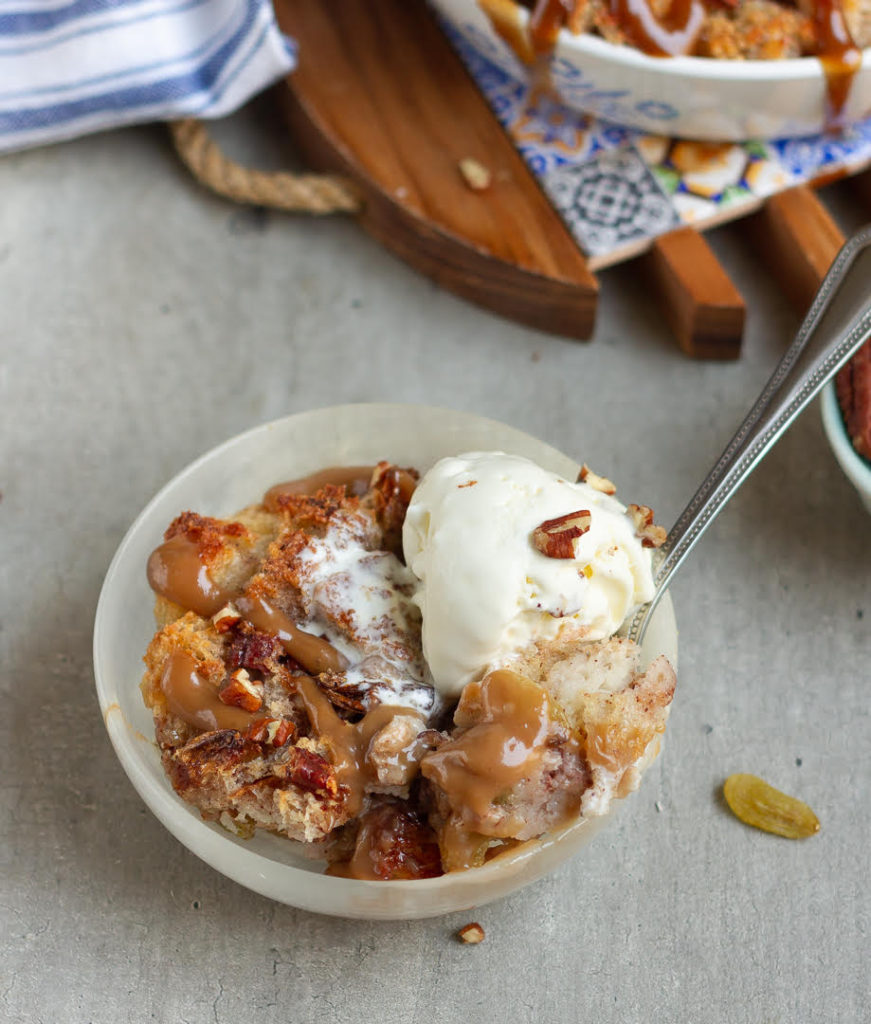 A spoon in a bowl of bread pudding with ice cream on top.