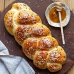 A braided loaf of bread with seeds on a wooden board with honey on the side.