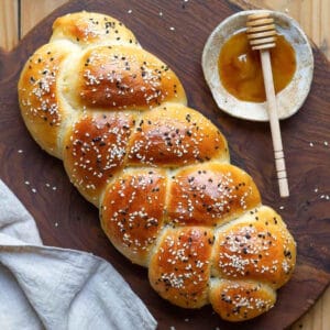 A braided loaf of bread with seeds on a wooden board with honey on the side.