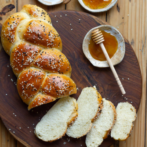 Sliced challah bread with honey on a wooden board.