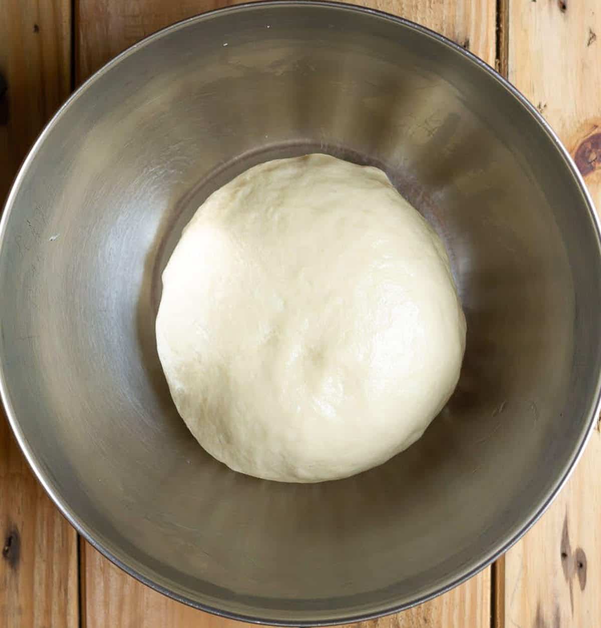 A ball of dough in a metal bowl.