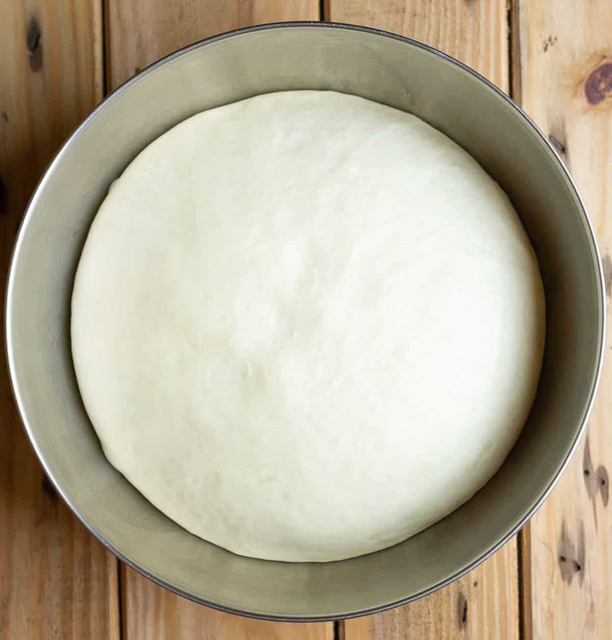 Proofed dough in a stainless steel mixing bowl.