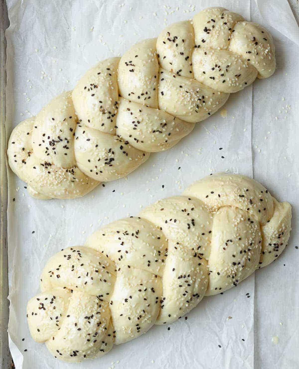 2 loaves of braided bread sprinkled with sesame seeds on parchment paper.