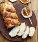 A loaf of bread with some slices on a wooden board with honey on the side.