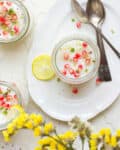 Jars of panna cotta with pomegranate arils, lemon slice, and yellow flowers.