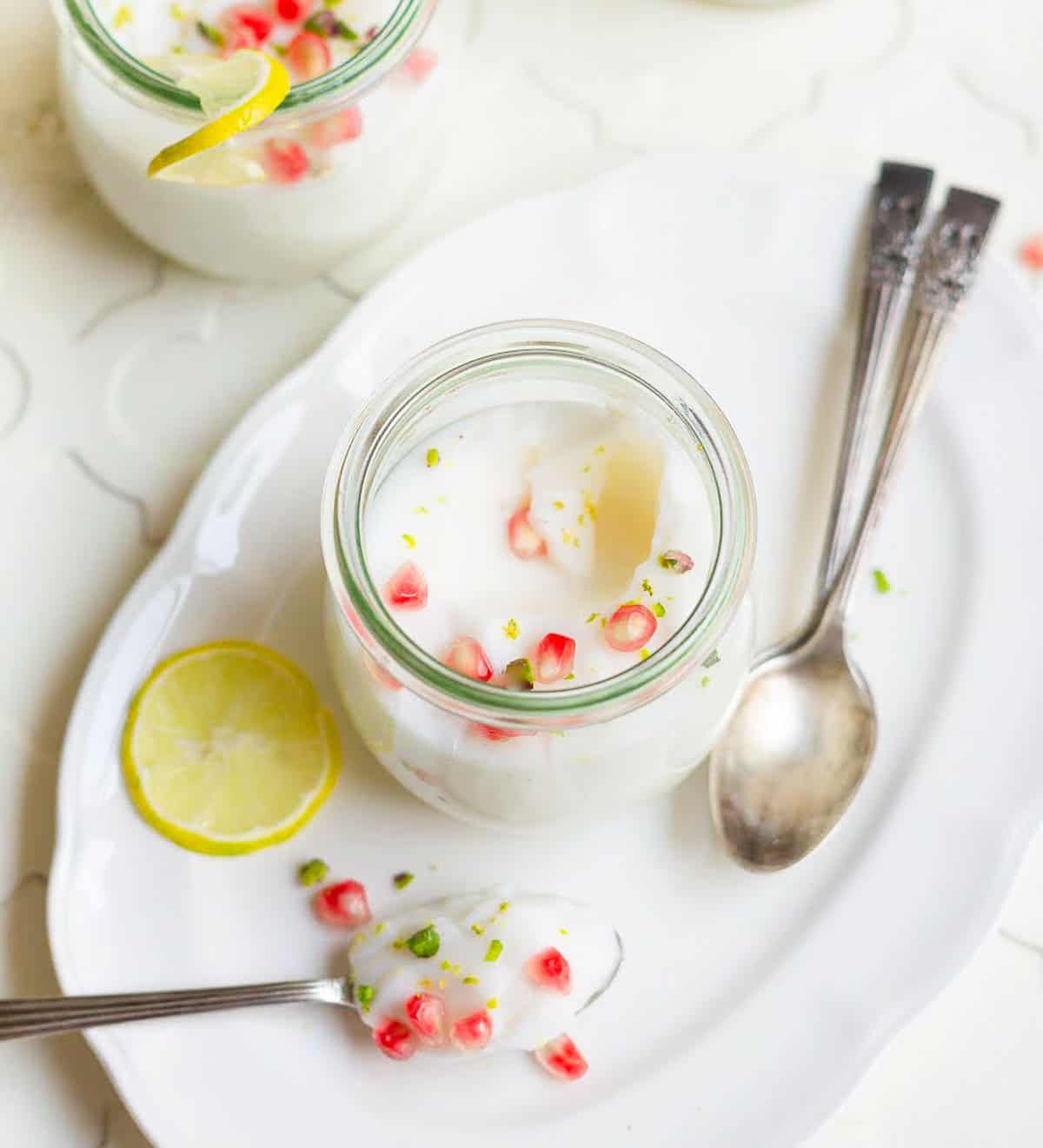 Panna cotta in a jar and a spoon with lemon slice and pomegranate seeds.