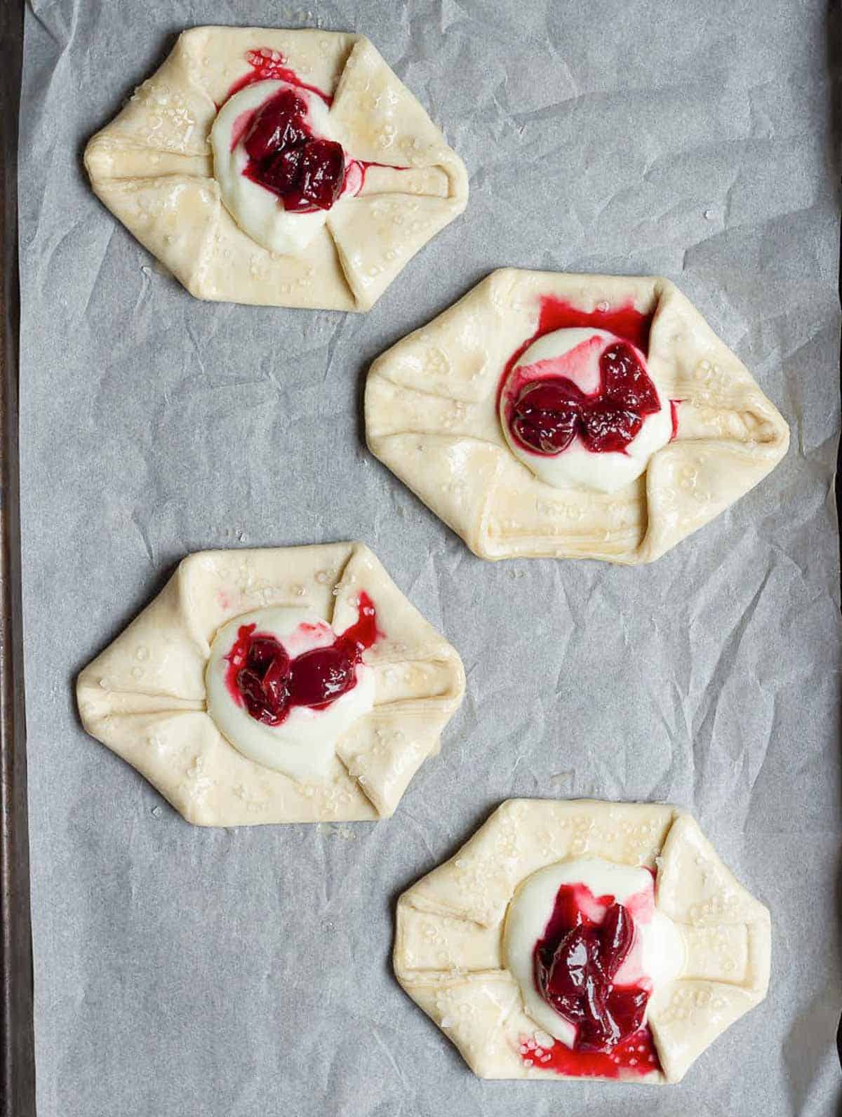 4 puff pastry pieces with cream cheese and cherry compote in the center of each.