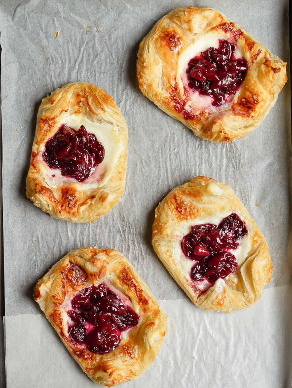 4 Baked puff pastry tarts with cream cheese and cherry compote on parchment paper.