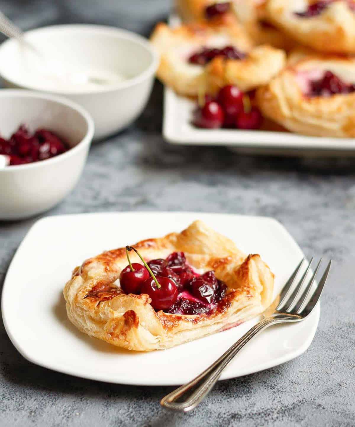 Cherry puff pastry tart on a small plate with fork.