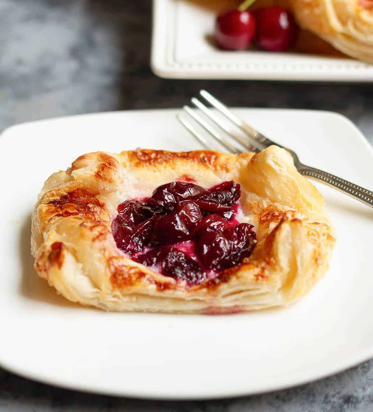 Puff pastry tart with cherries on a small white plate.