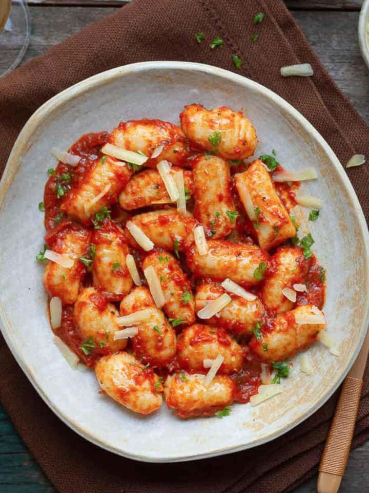 Gnocchi with tomato sauce on a plate topped with cheese, with a fork on the side.