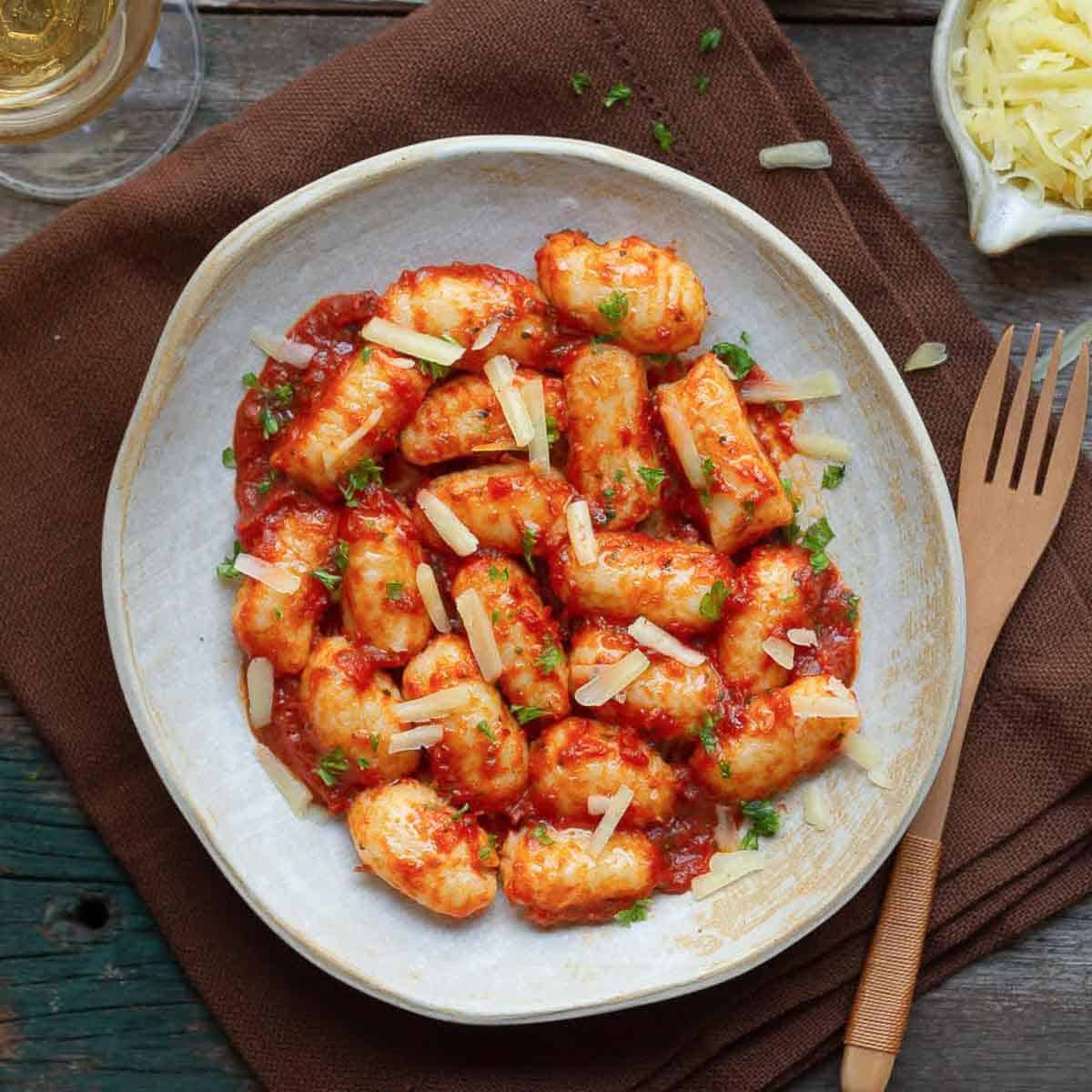 Gnocchi with tomato sauce on a plate topped with cheese, with a fork on the side.