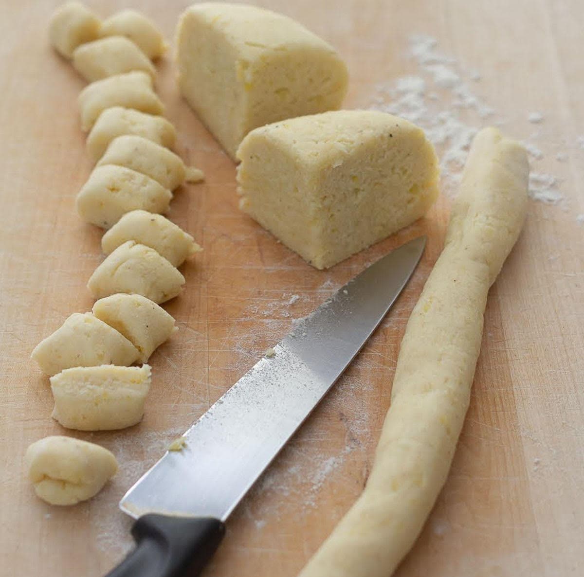 Dough shaped into a rope and cut into pieces on a wooden board with a knife on it.