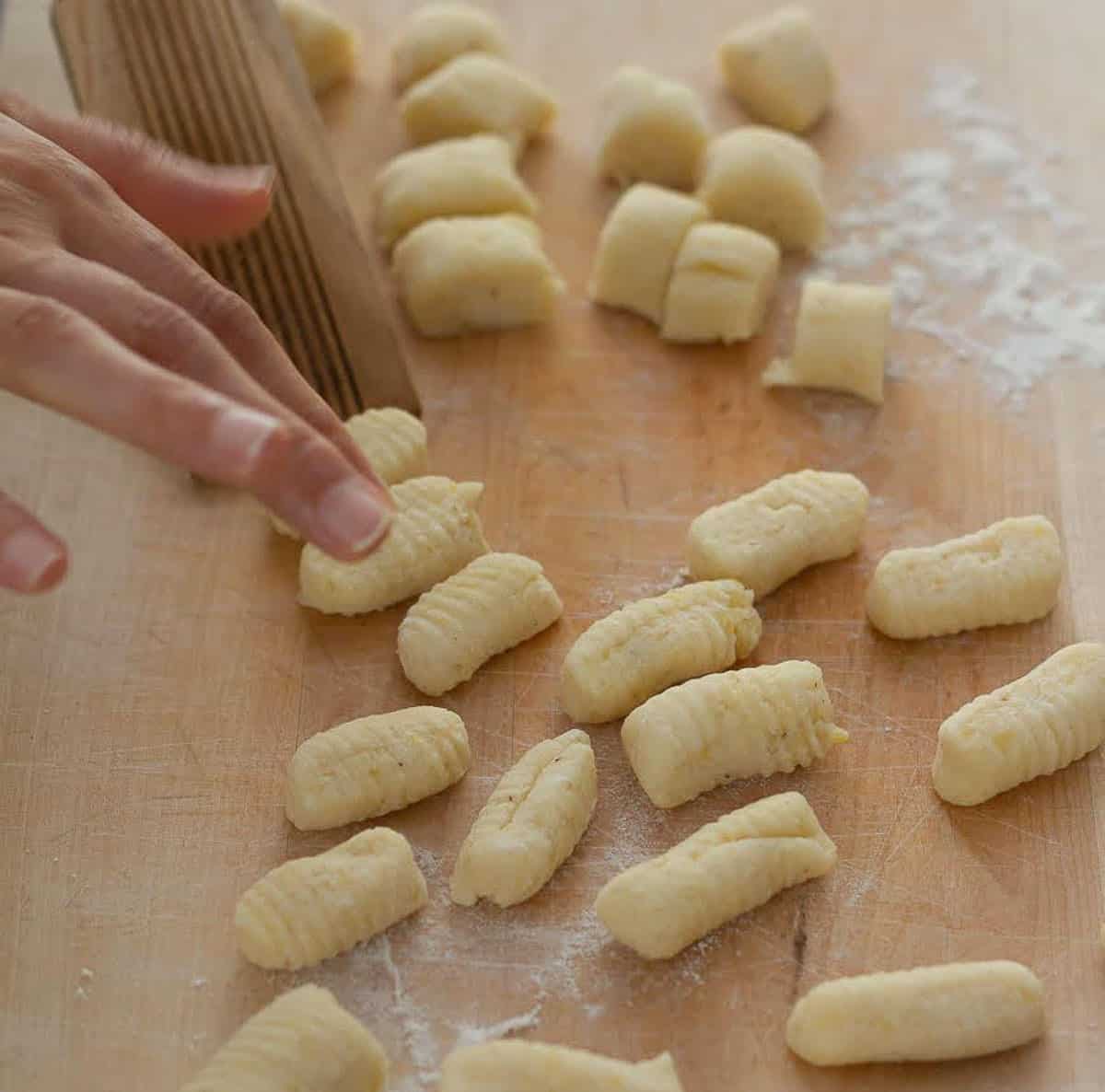 A hand shaping gnocchi on a gnocchi board.