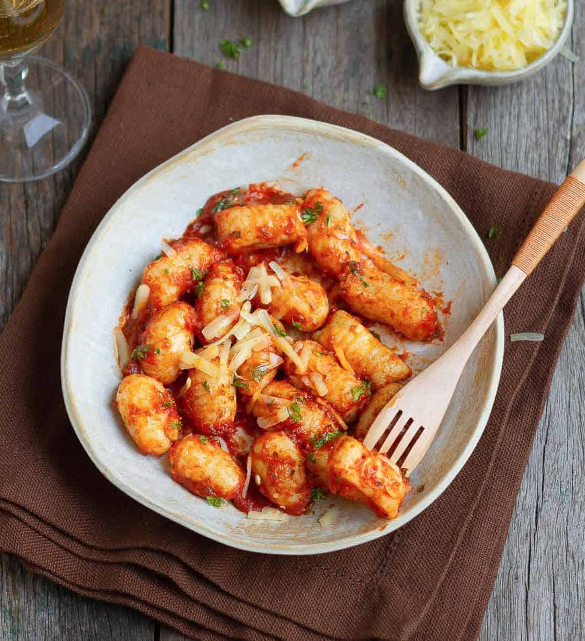Tomato sauce gnocchi on a plate with a fork holding a gnocchi.