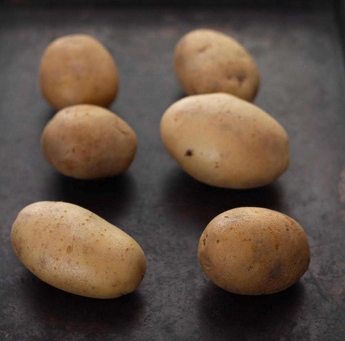 Potatoes on a black baking tray.