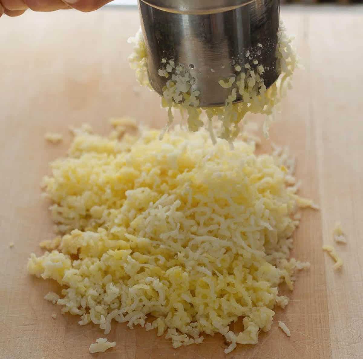 A potato ricer shredding potato on a pile of shredded potatoes.