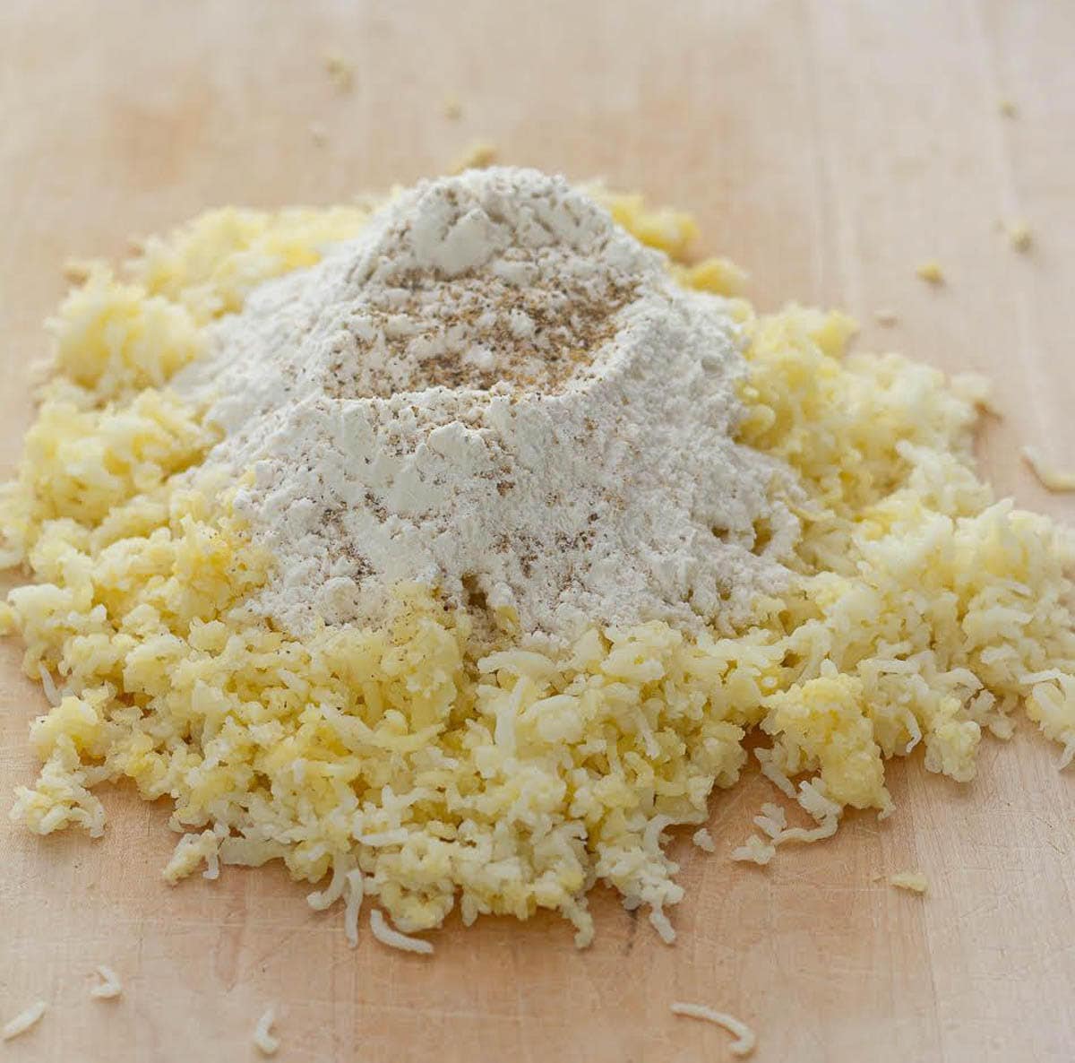 Riced potatoes with flour, salt, and pepper on top on a wooden board.