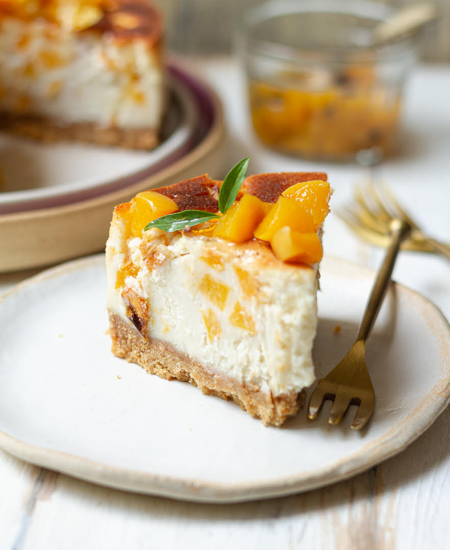 A slice of cheesecake with peaches on a small plate with a fork.