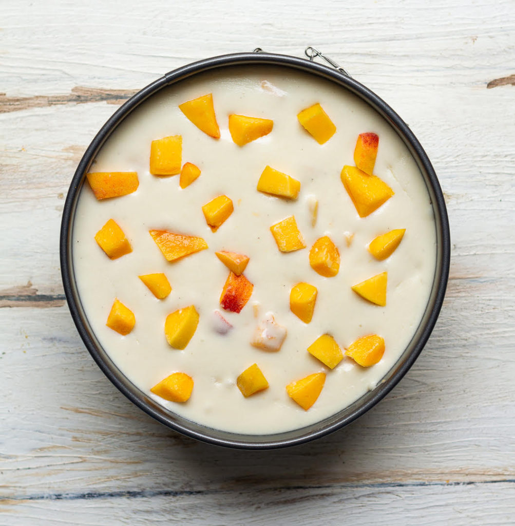 Cheesecake batter with chopped peaches on top in a cake pan.
