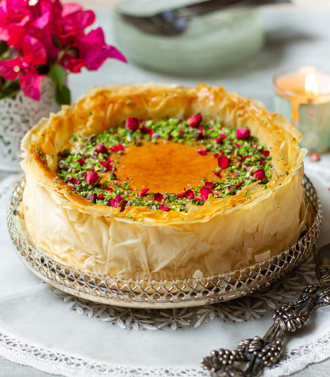 Baklava-style cheesecake on a silver platter with flowers and a candle.