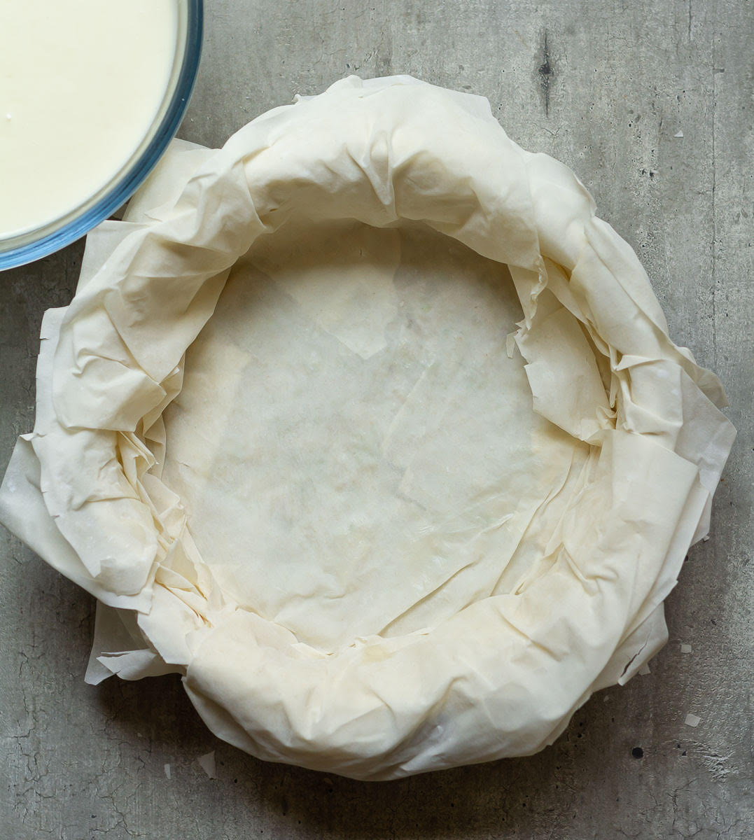 Phyllo pastry crust in a round pan with cheesecake batter on the side.