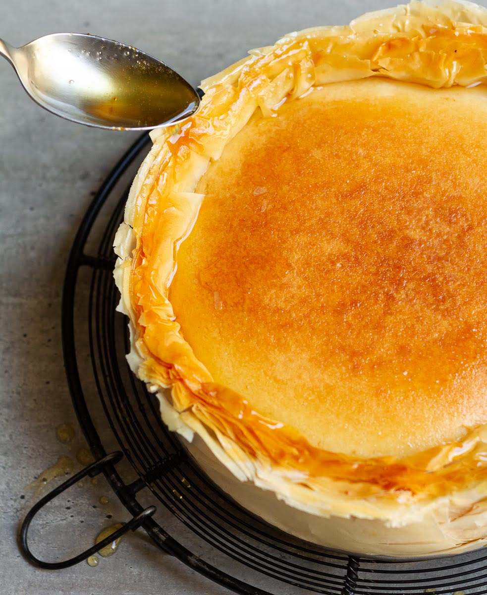 A spoon pouring syrup on the cheesecake crust.