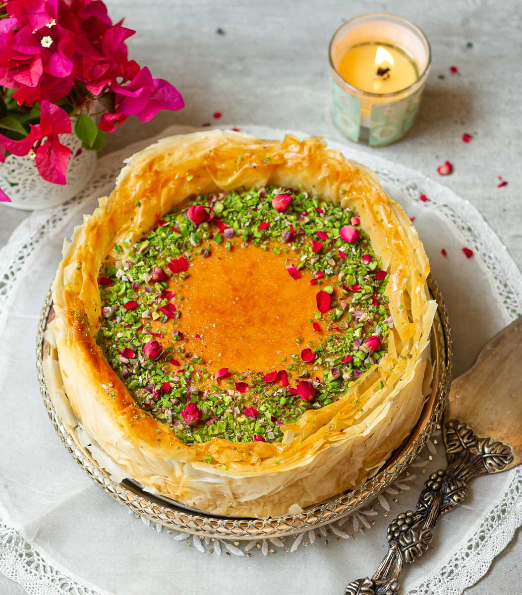 Cheesecake with phyllo pastry on a platter with a cake server, candle and flowers.