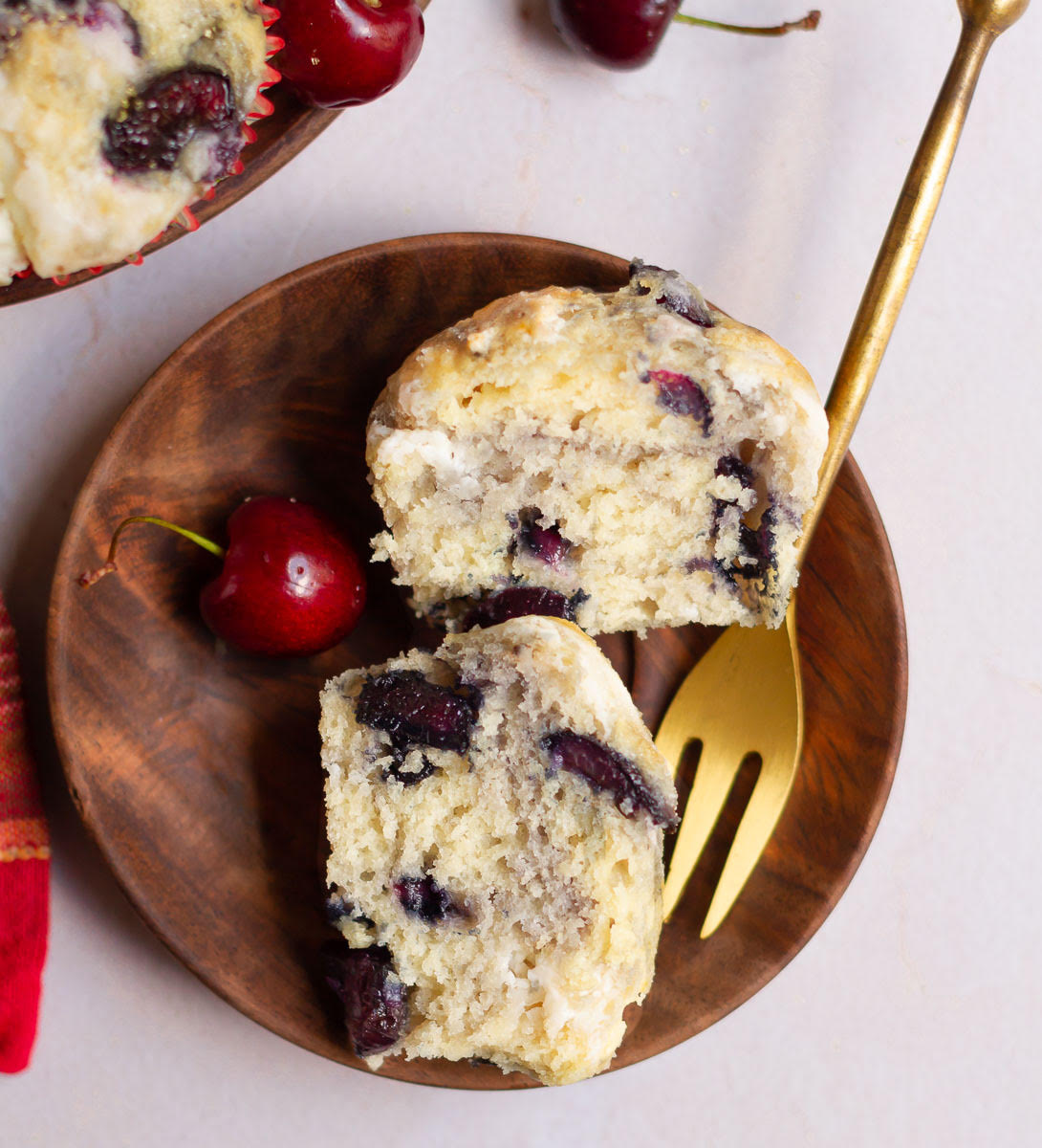 2 halves of a cherry muffin on a small wooden plate with a fork.