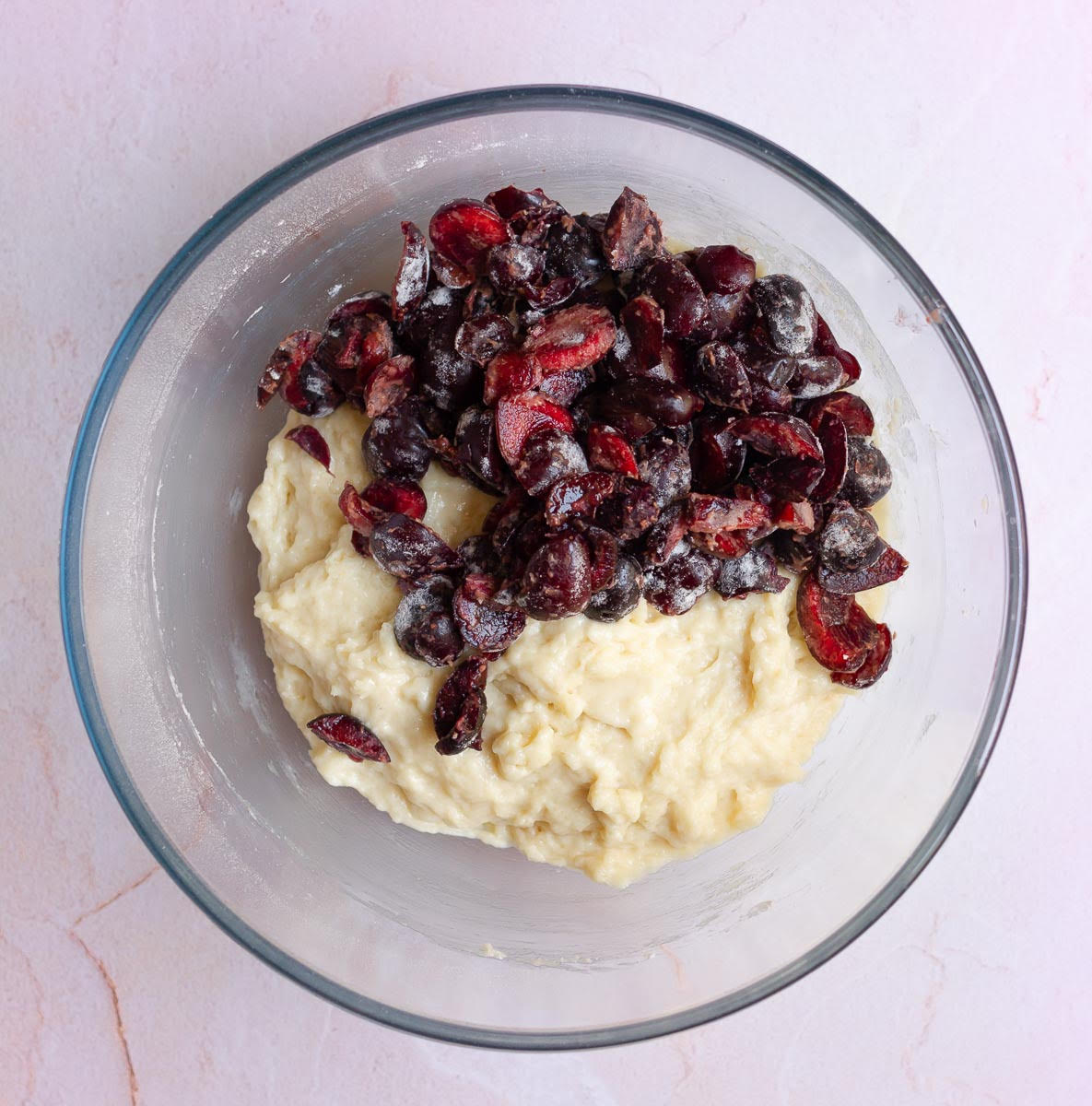 Sliced cherries on top of batter in a mixing bowl.