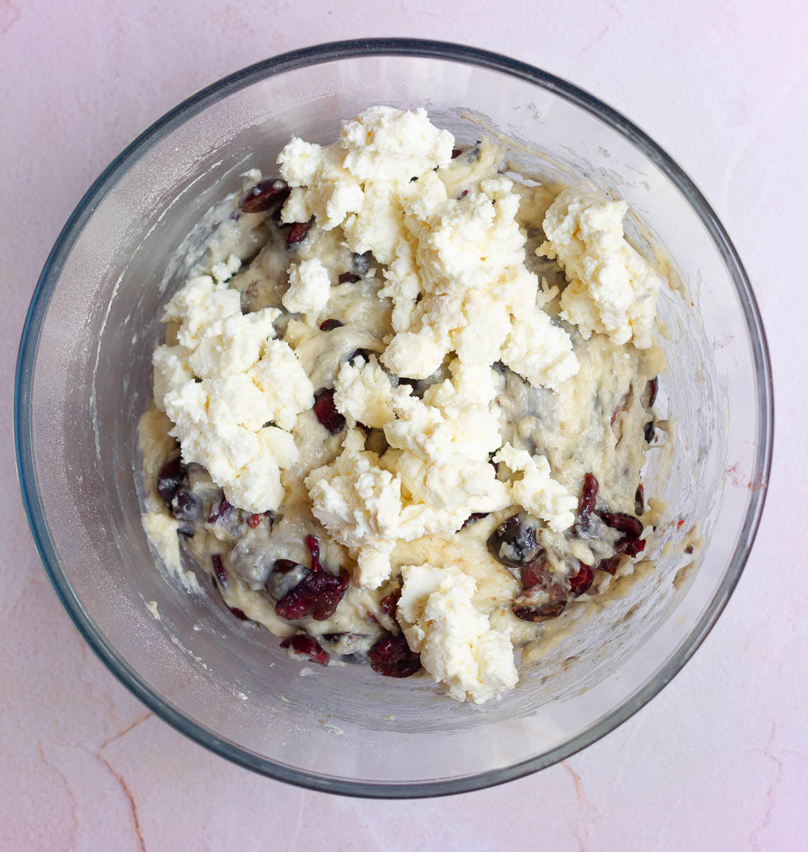 Cream cheese pieces on top of cherry muffin batter in a mixing bowl.