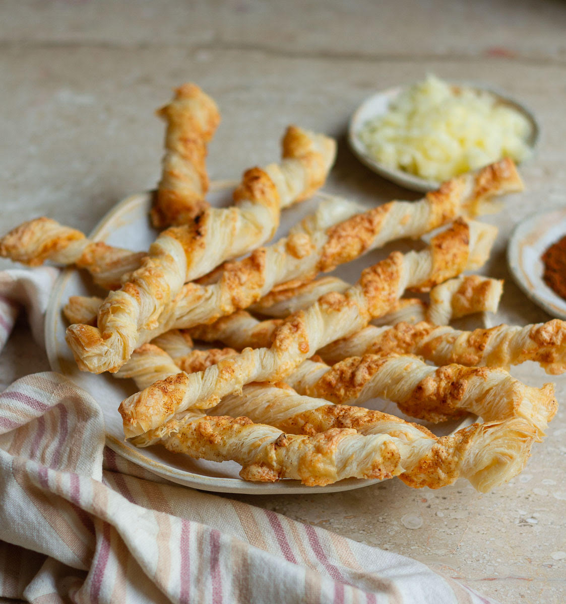 cheese straws on a serving plate with shredded cheese in the background.