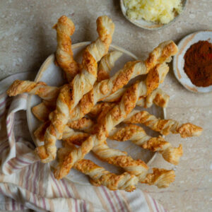Cheese straws in a bowl with ingredients around.