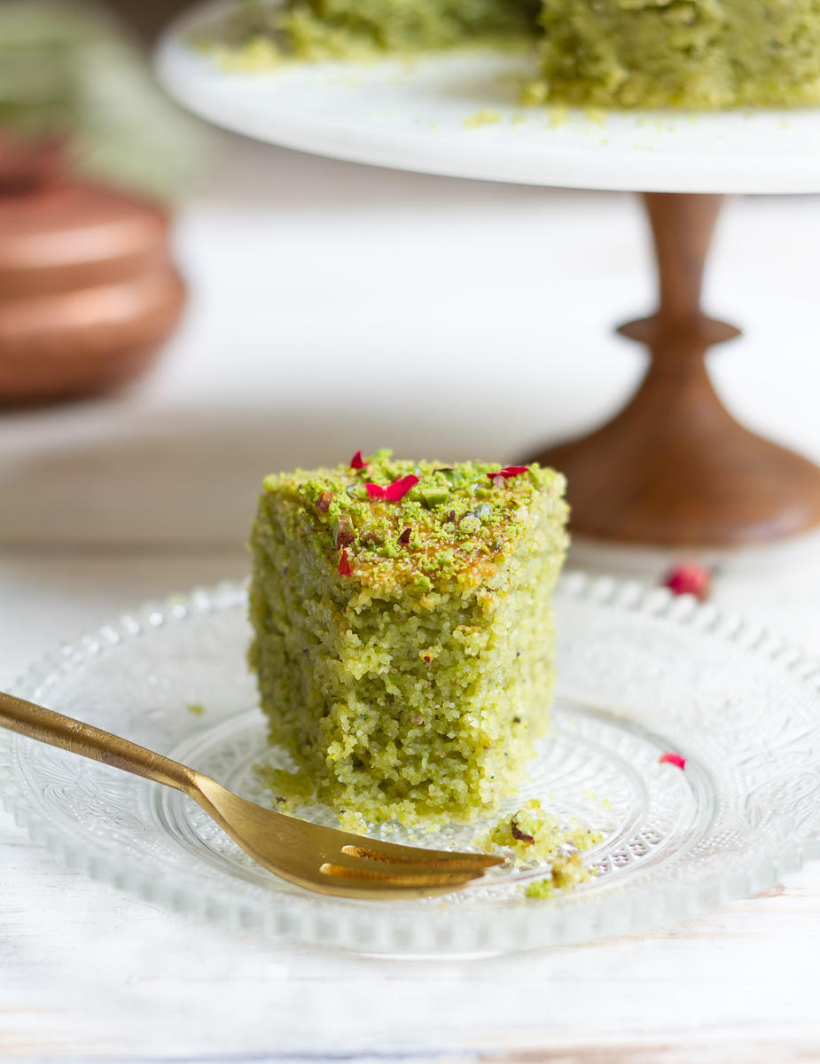 A bite taken off a slice of pistachio cake on a plate with a fork.
