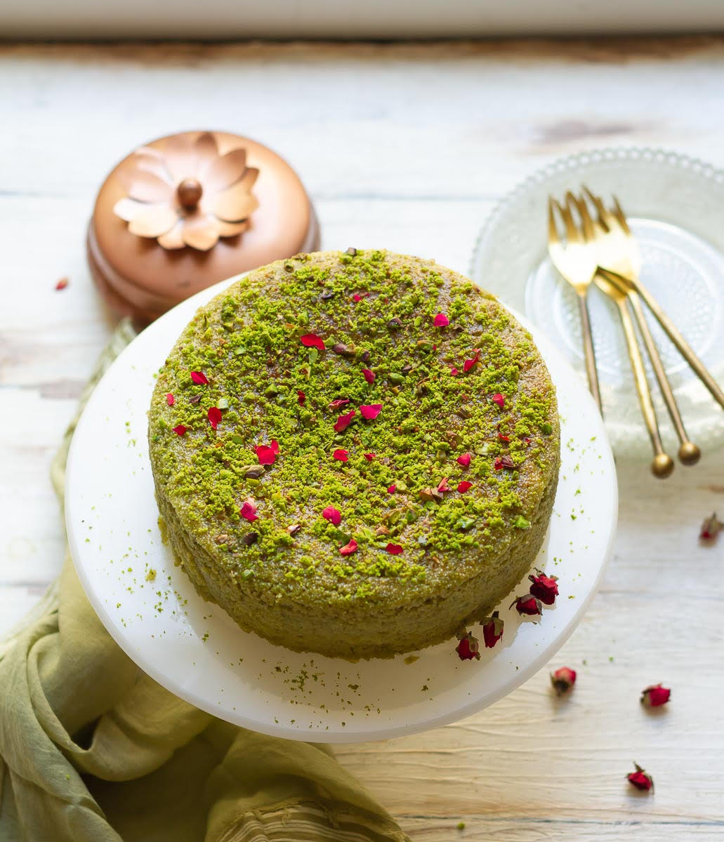 Pistachio cake on a cake stand with rose petals on top.